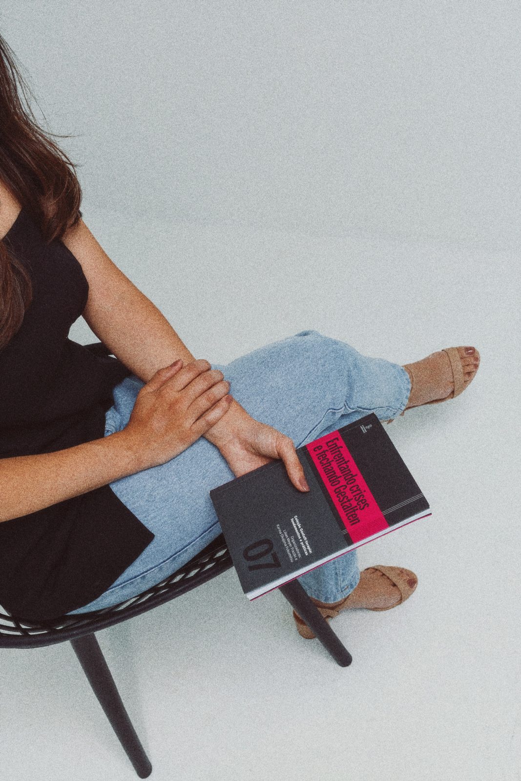Amanda Rafaelly sentada com um livro apoiado sobre as pernas, em ambiente claro